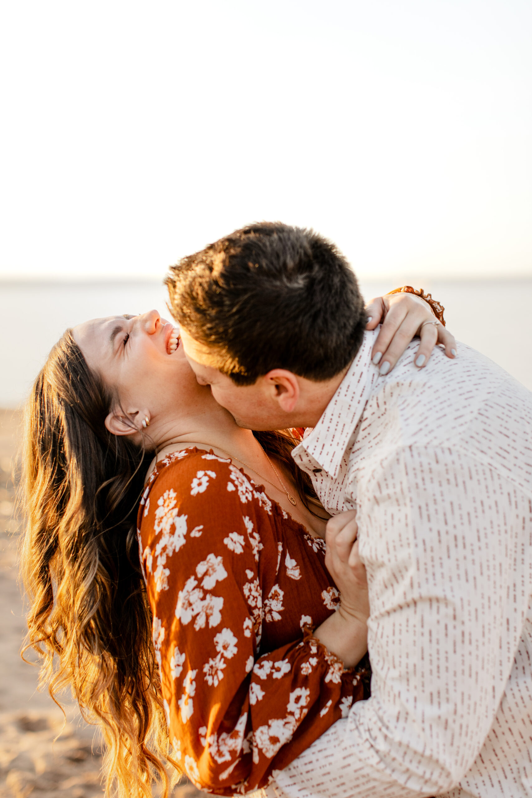 Couple giggling on the beach near Lake Superior, during their engagement session with Morgan Elizabeth Photography. Learn more at www.morganelizabethphoto.com