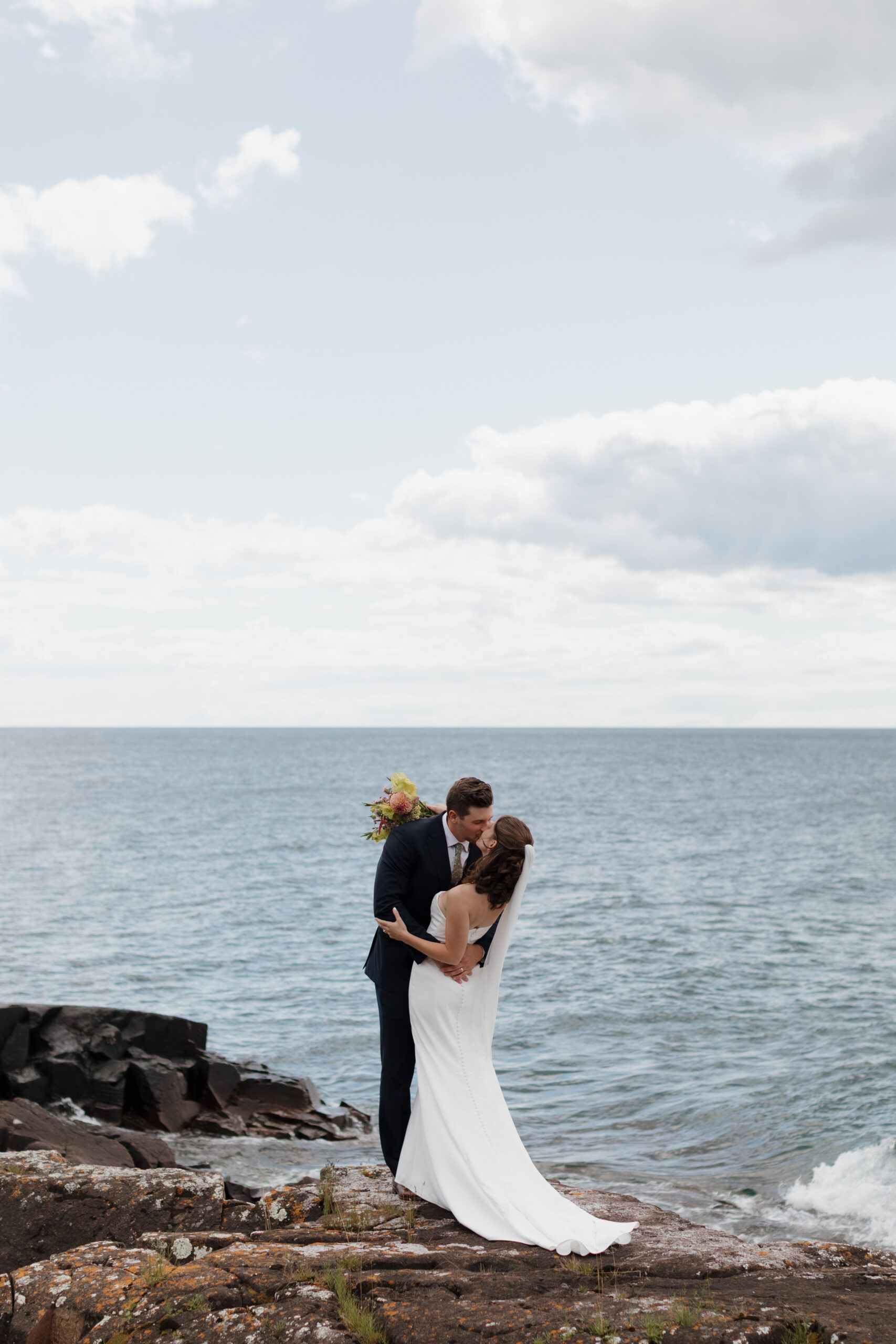 a couple kissing next to the water on the day of their wedding next to the water in Grand Marais, Minnesota