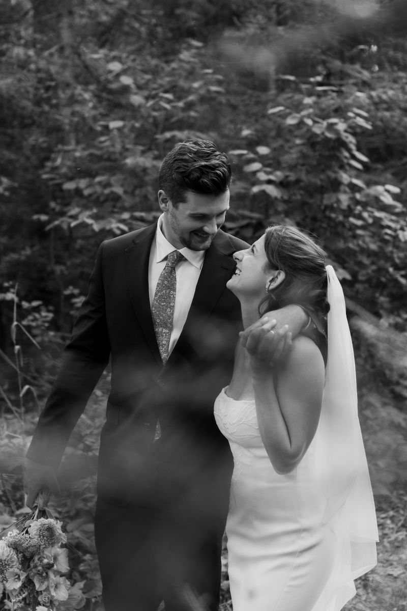 a couple smiling at each other and walking down a trail together with their arms wrapped around each other