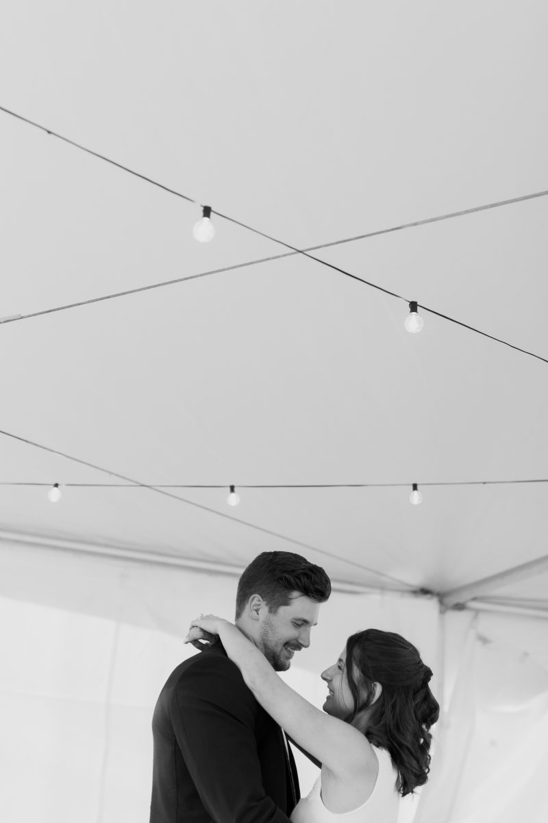 a couple sharing a first dance underneath a tent during their backyard wedding 