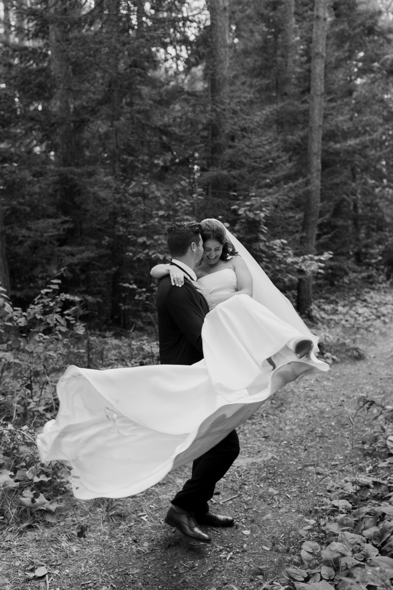 a groom picking up his bride on a wooded trail