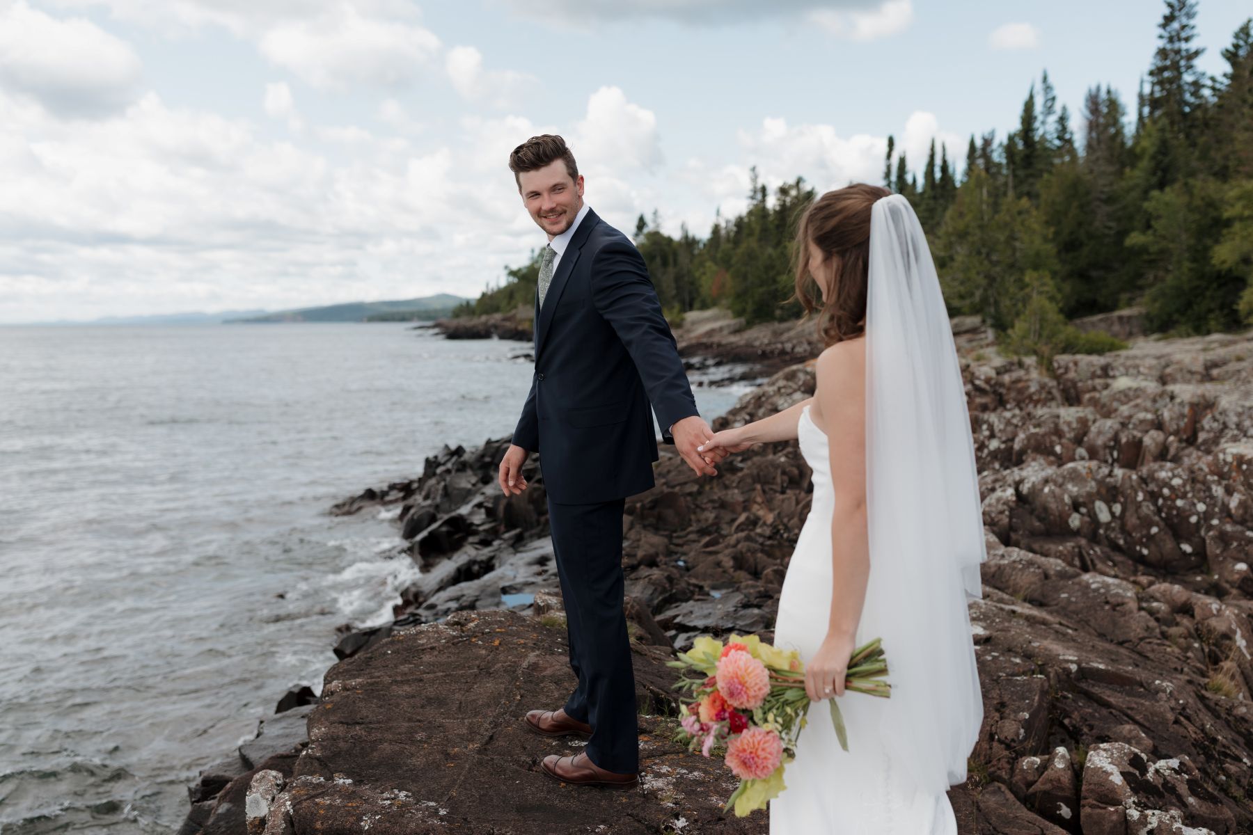 a couple holding hands and smiling at each other standing next to the water 