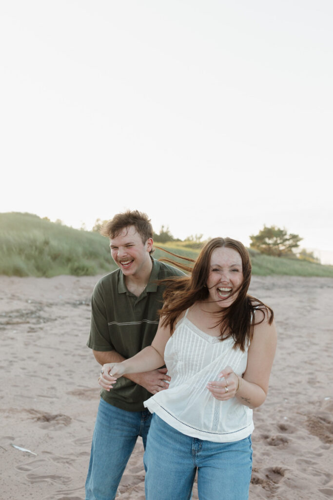 A couple laughing on the beach as one holds the other's waist 