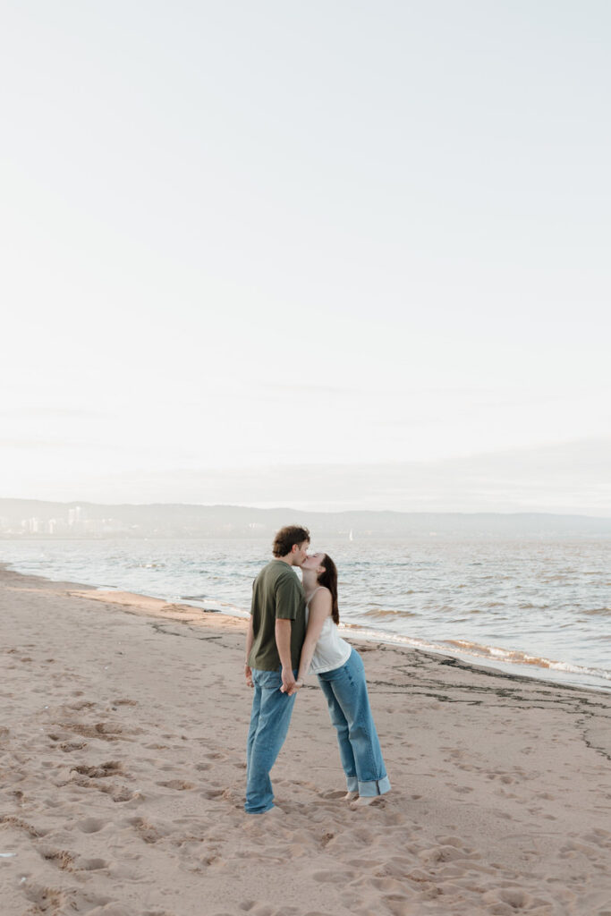 A person leaning into their partner and kissing them while holding hands 