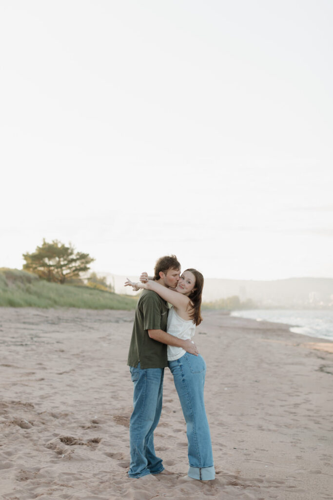 A couple with their arms around each other as one kisses the other's cheek 