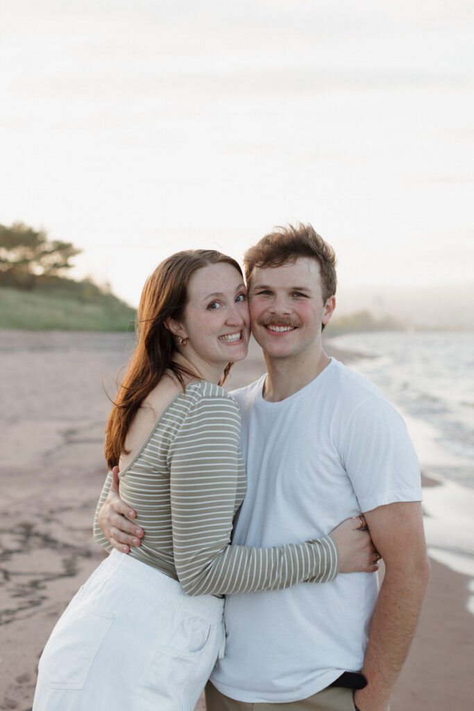 A couple hugging and smiling on the beach while standing cheek to cheek 
