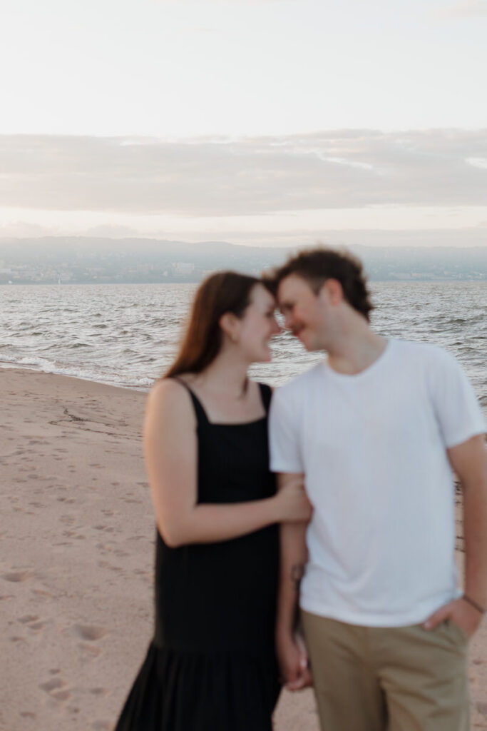 A couple standing forehead to forehead smiling at each other on the beach 

