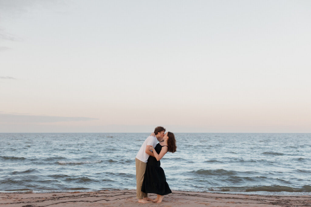 A person leaning into their partner as they kiss at sunset on the beach 