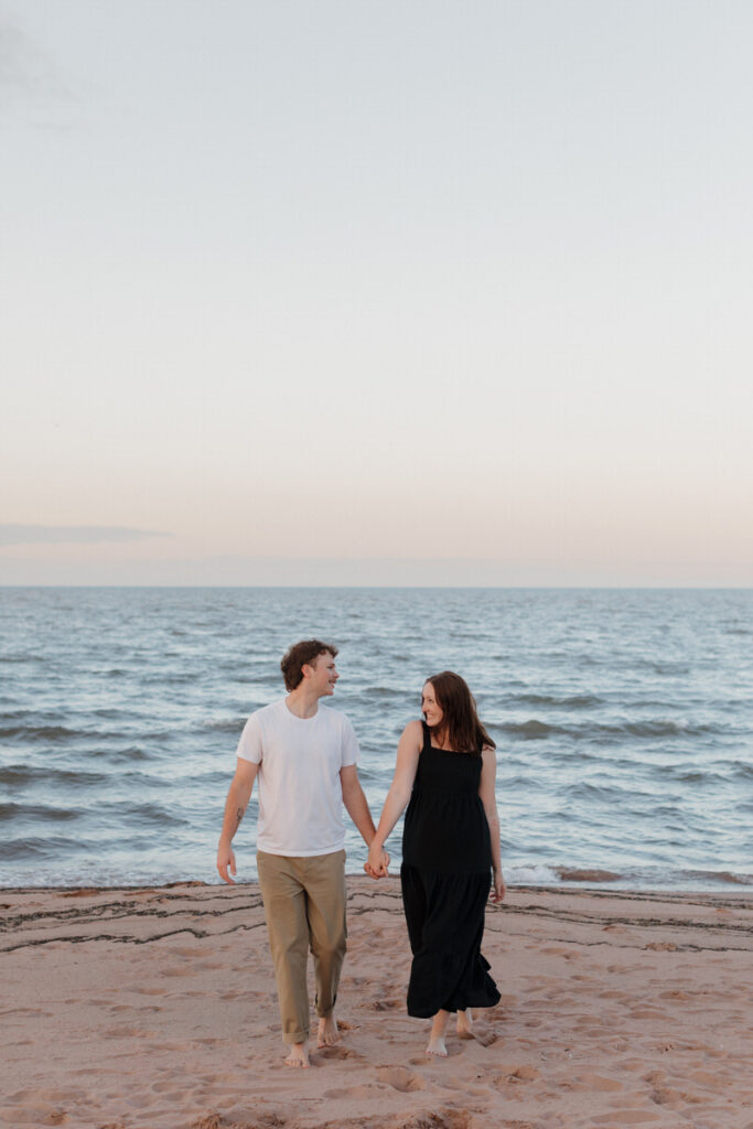 A couple holding hands and smiling at each other while walking on the beach 
