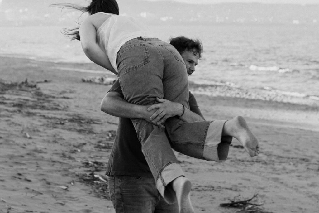 A person carrying their partner over their shoulder on the beach 