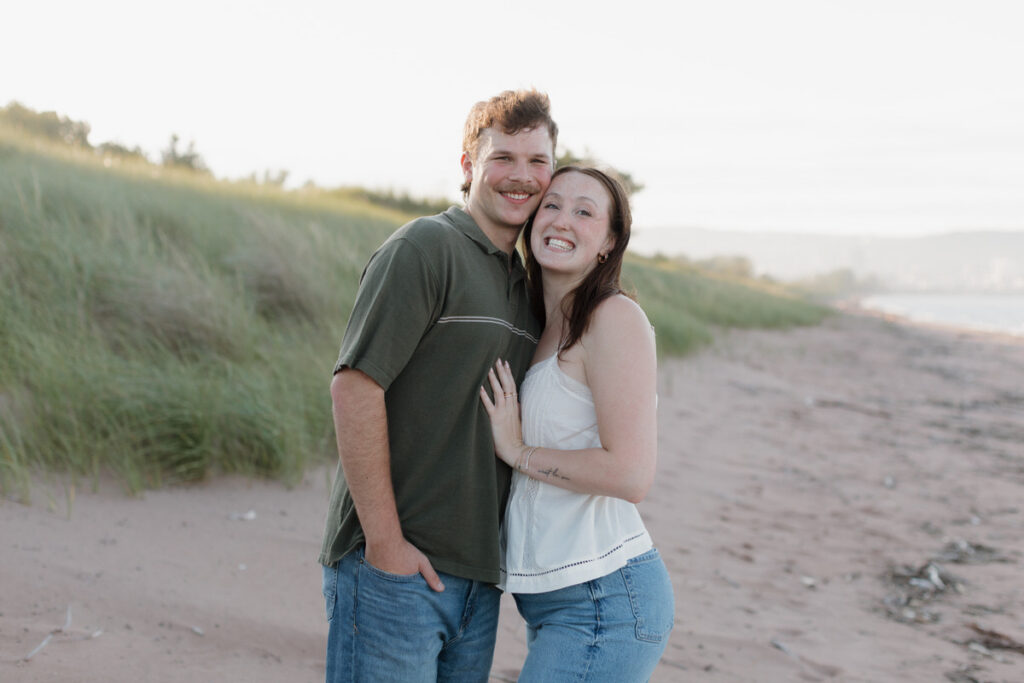A couple standing close together smiling at the beach 