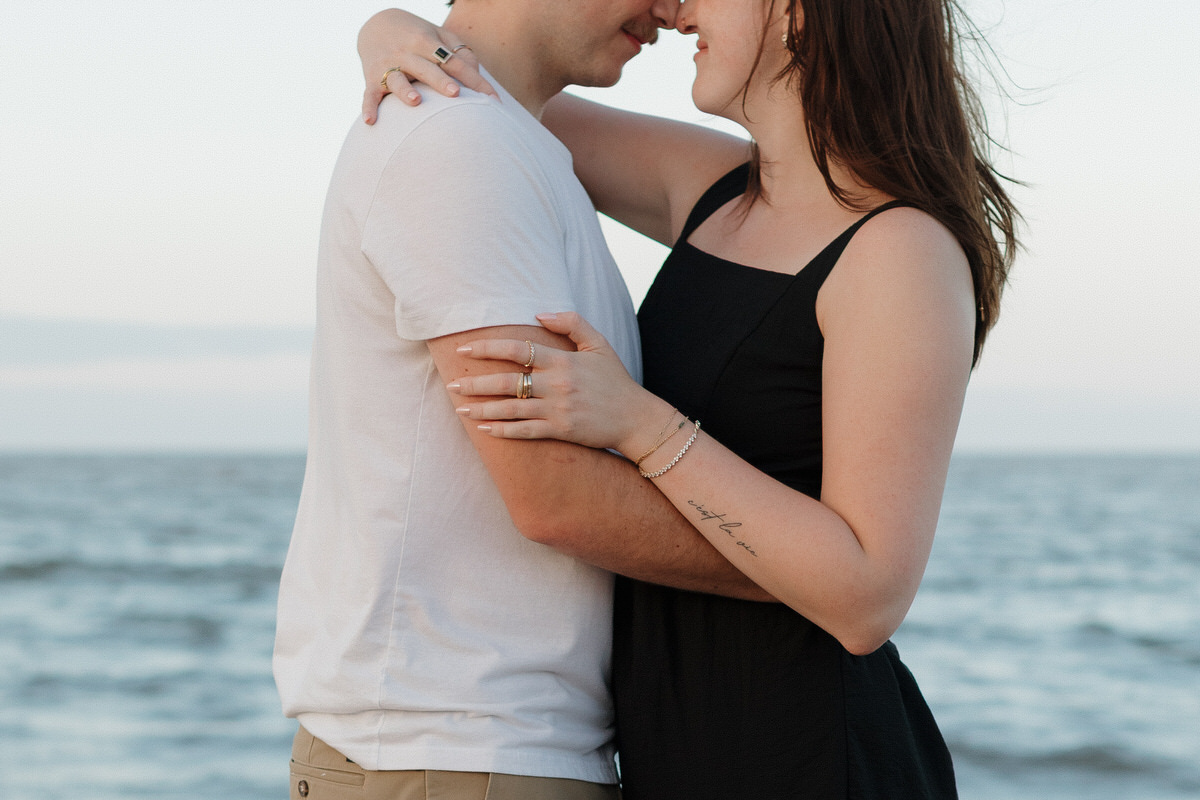A couple standing head to head with their arms around each other during their couples photo session on the beach