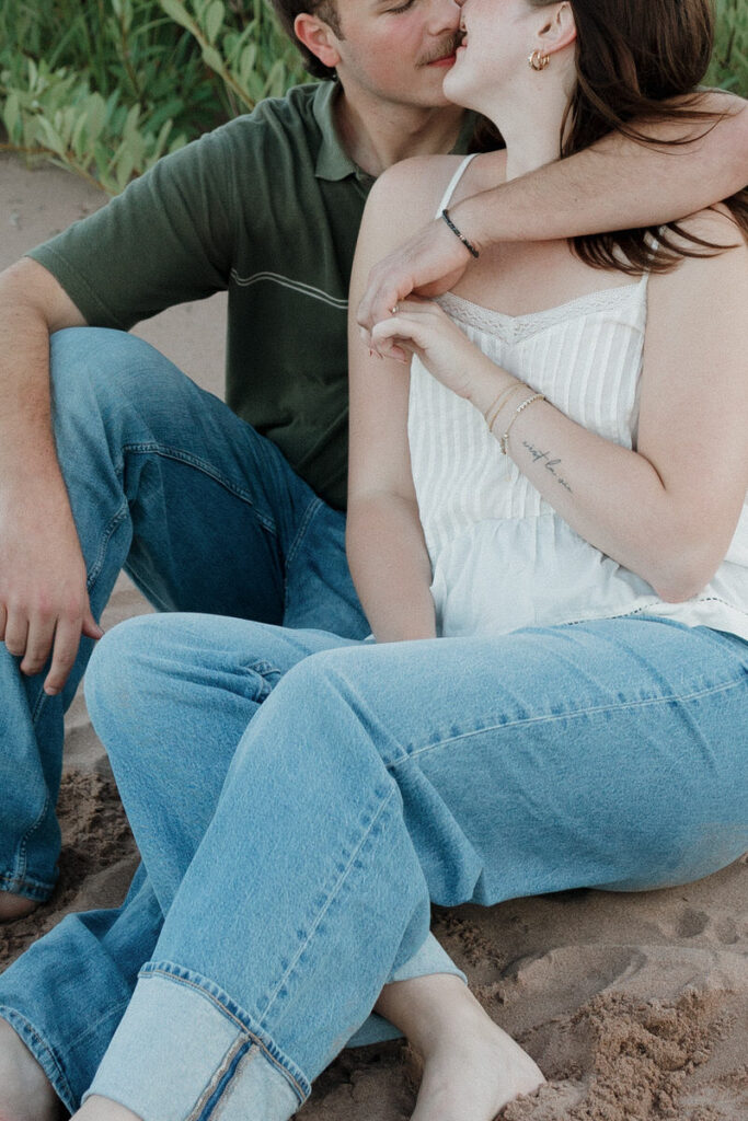 A couple sitting on the beach together with their arms around each other about to kiss
