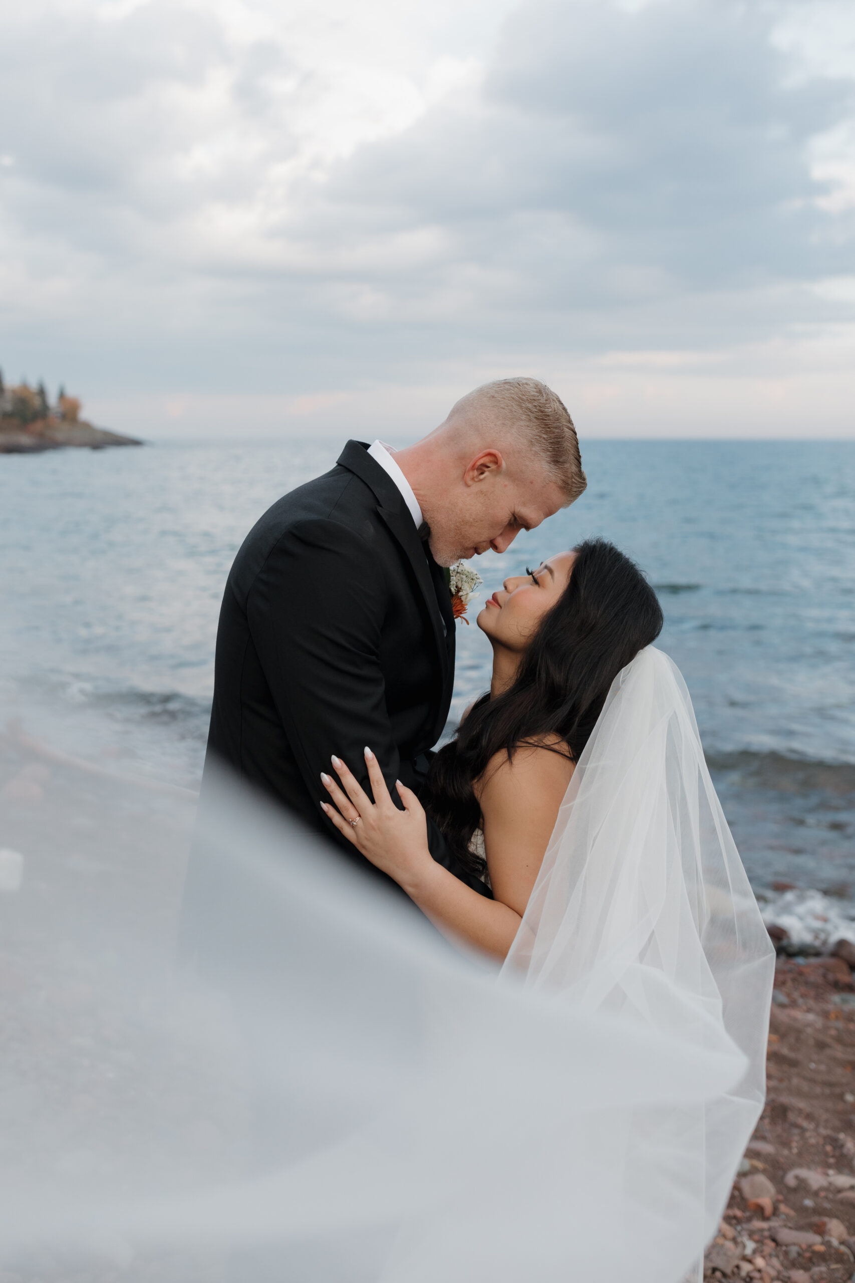 a couple taking wedding portraits next to lake superior the bride's veil is blowing in the wind 