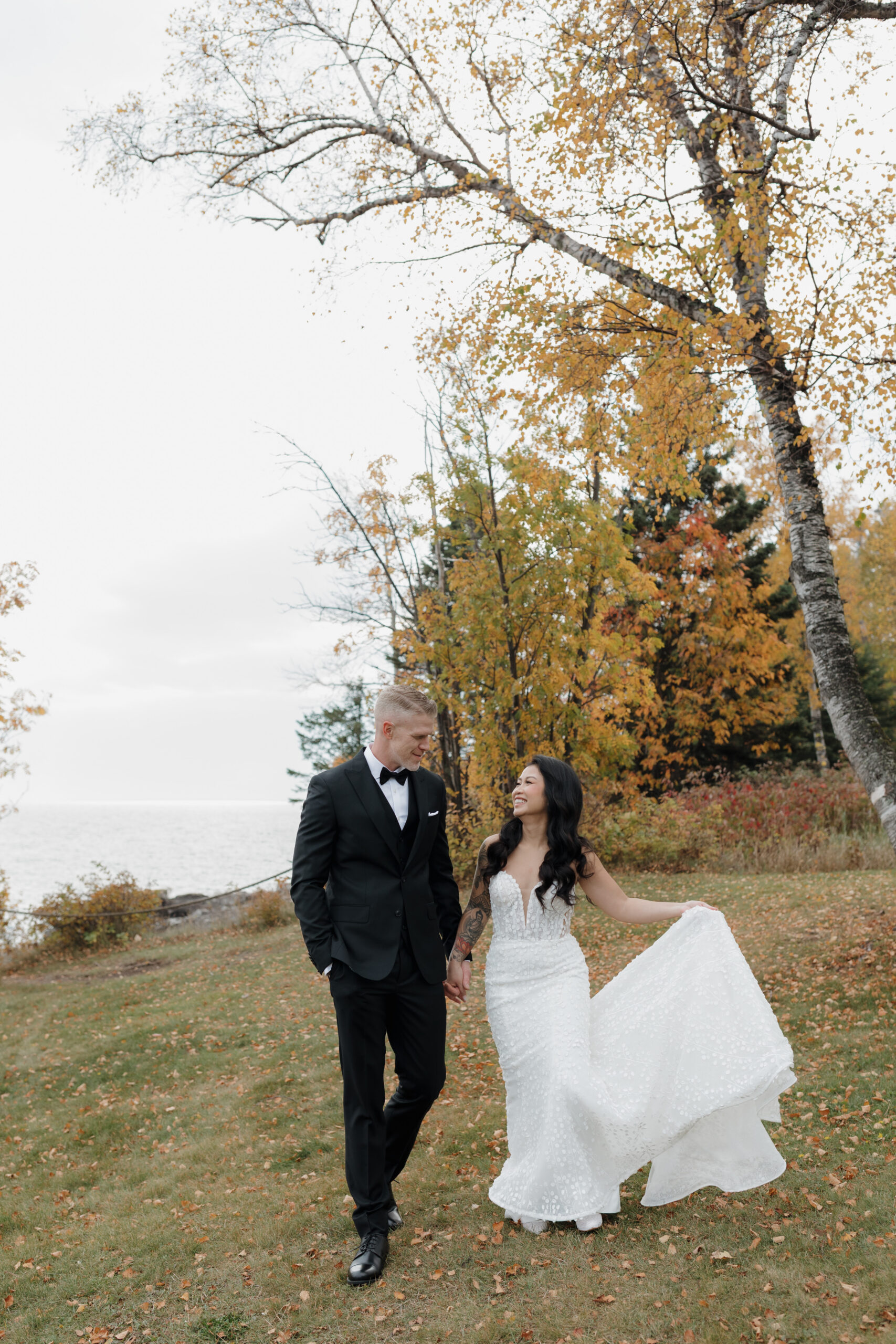 a copule taking wedding portraits at bluefin bay in tofte mn they are walking on a hill and surrounded by fall foliage 